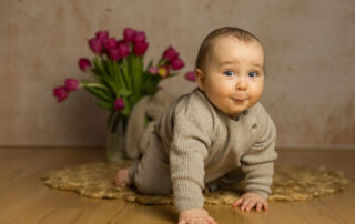 Fröhlich grinsendes Baby krabbelt auf die Kamera zu vor einer frühlingshaften Tulpenkulisse