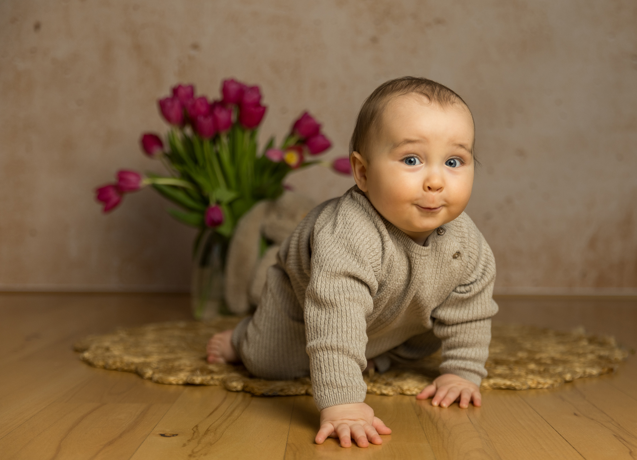 Fröhlich grinsendes Baby krabbelt auf die Kamera zu vor einer frühlingshaften Tulpenkulisse