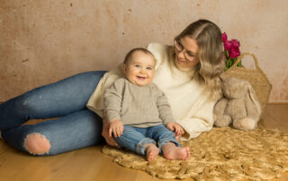 Mutter und Baby sitzen auf dem Boden und lachen glücklich in die Kamera