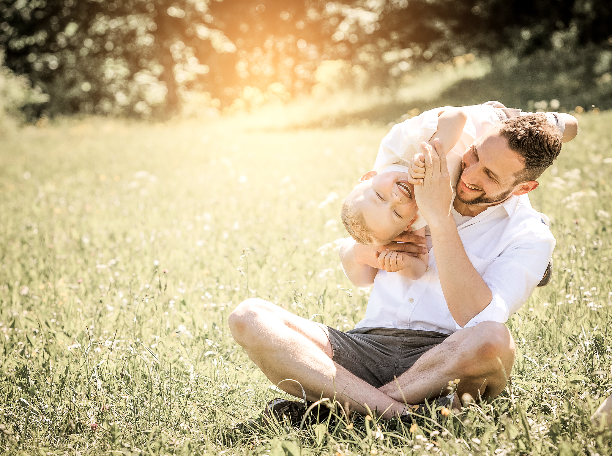 Papa und Sohn spielen lachend auf der Wiese, lebendige Familienfotografie in der Natur.