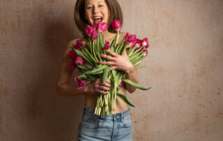 Junge Frau springt fröhlich in die Luft, hält dabei einen Strauss Tulpen im arm