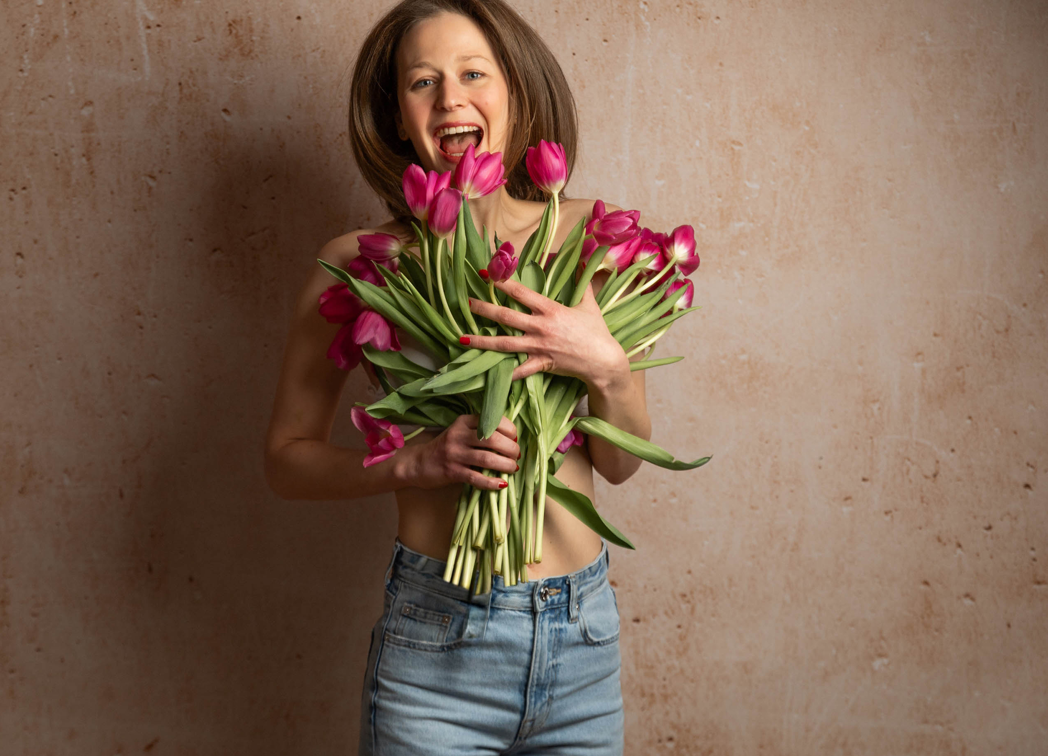 Junge Frau springt fröhlich in die Luft, hält dabei einen Strauss Tulpen im arm