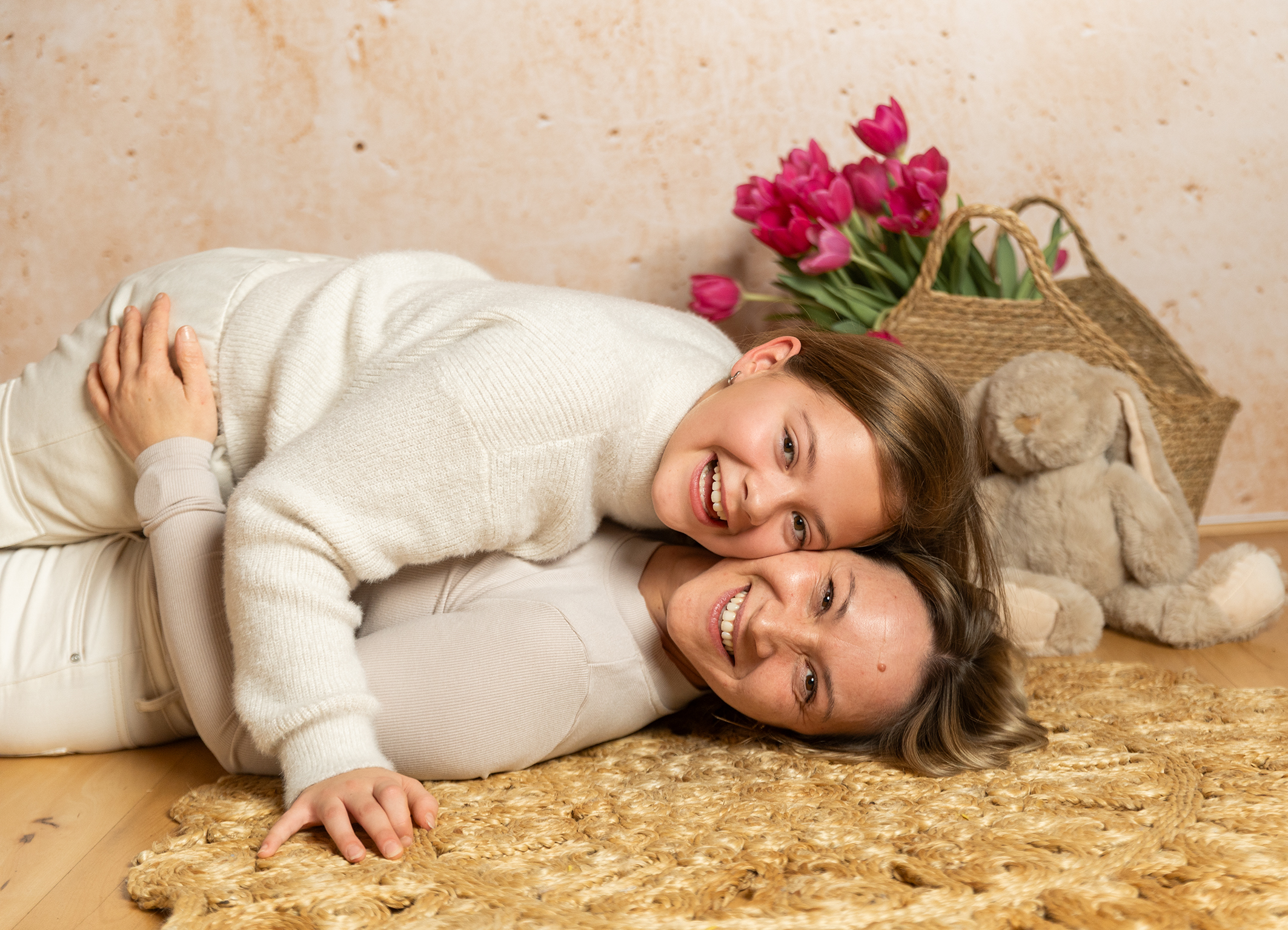 Mutter und Tochter kuscheln lachend im neben einem Korb mit Tulpen und einem kleinen Osterhasen