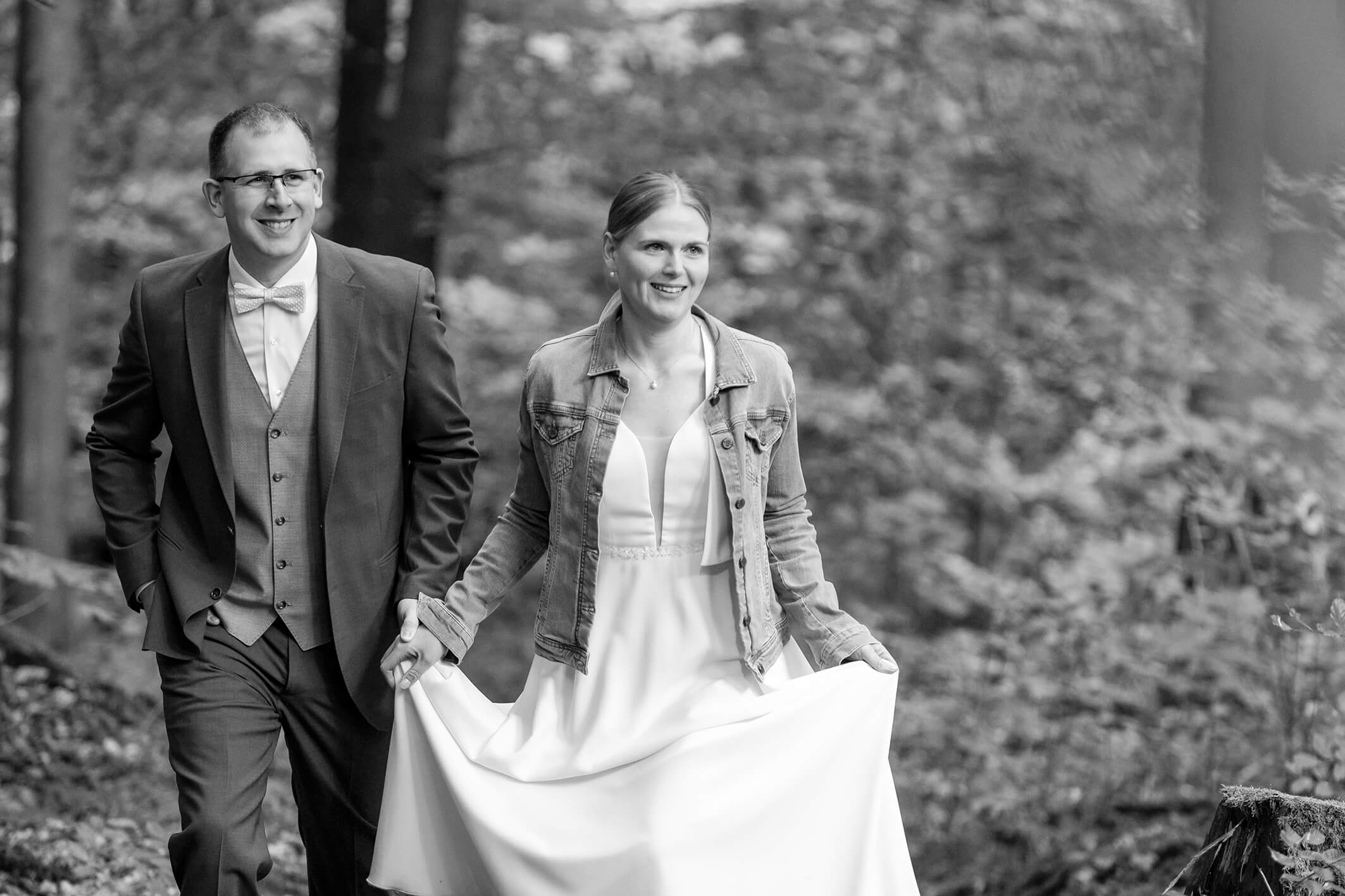 Schwarz weiß Portrait eines Brautpaares im Wald, Blätter rahmen das Paar ein, sie küssen sich.