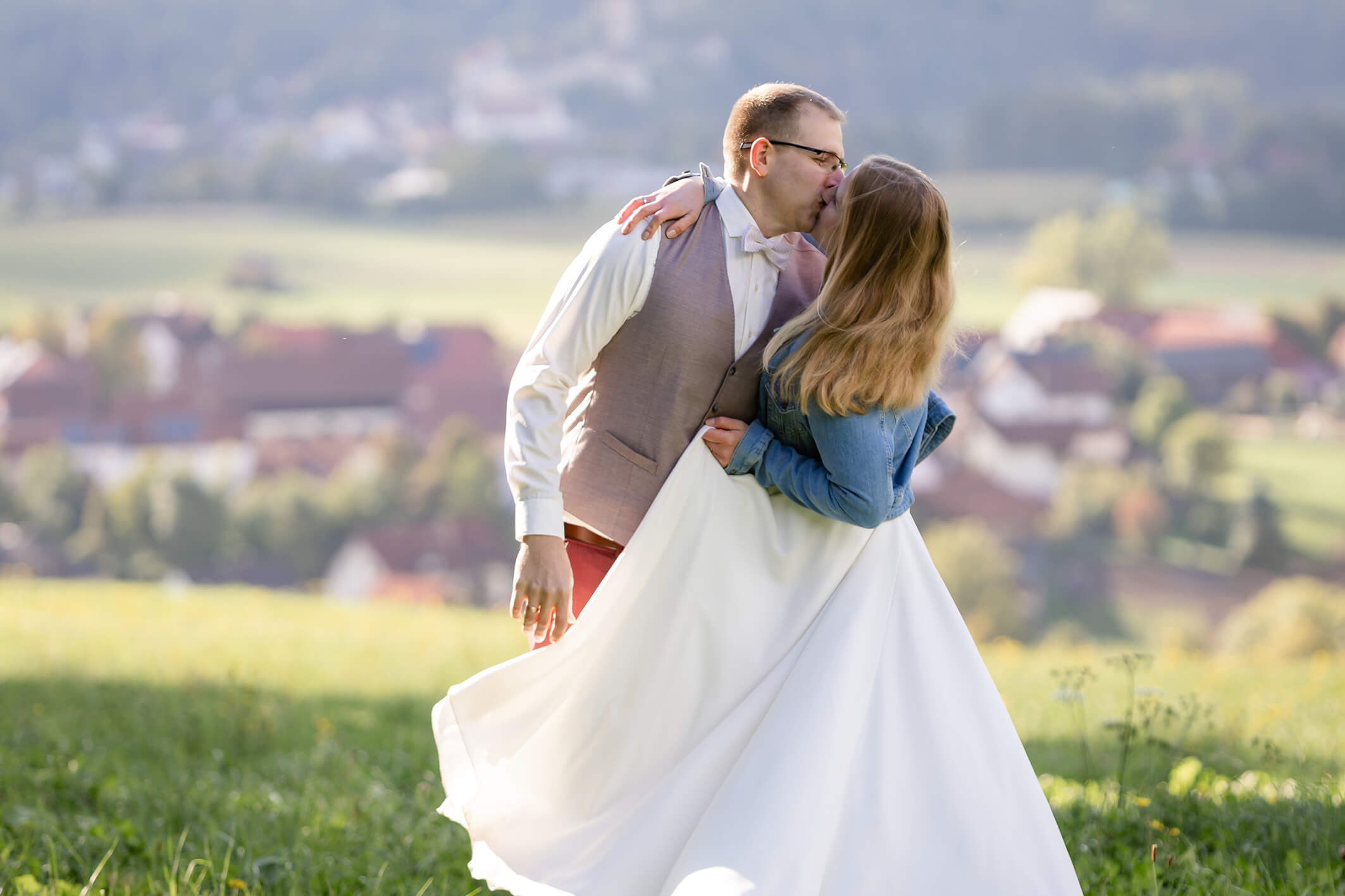 Brautpaar steht auf einer Wiese und küsst sich, weicher Hintergrund und ruhige Bildstimmung.