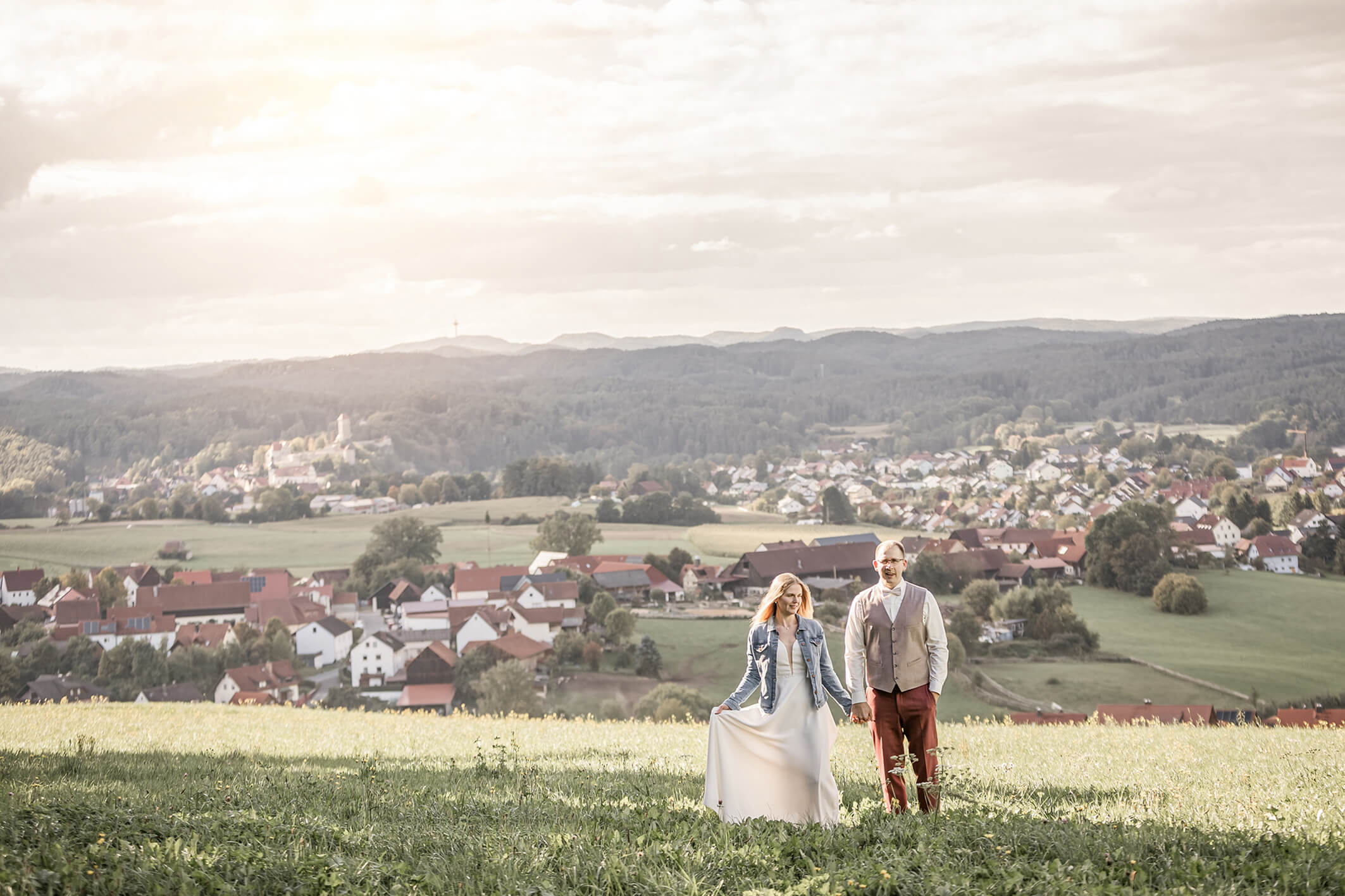 Brautpaar auf einer Wiese mit Blick auf die Burg Veldenstein in Neuhaus, romantische Hochzeitsaufnahme in der Natur.