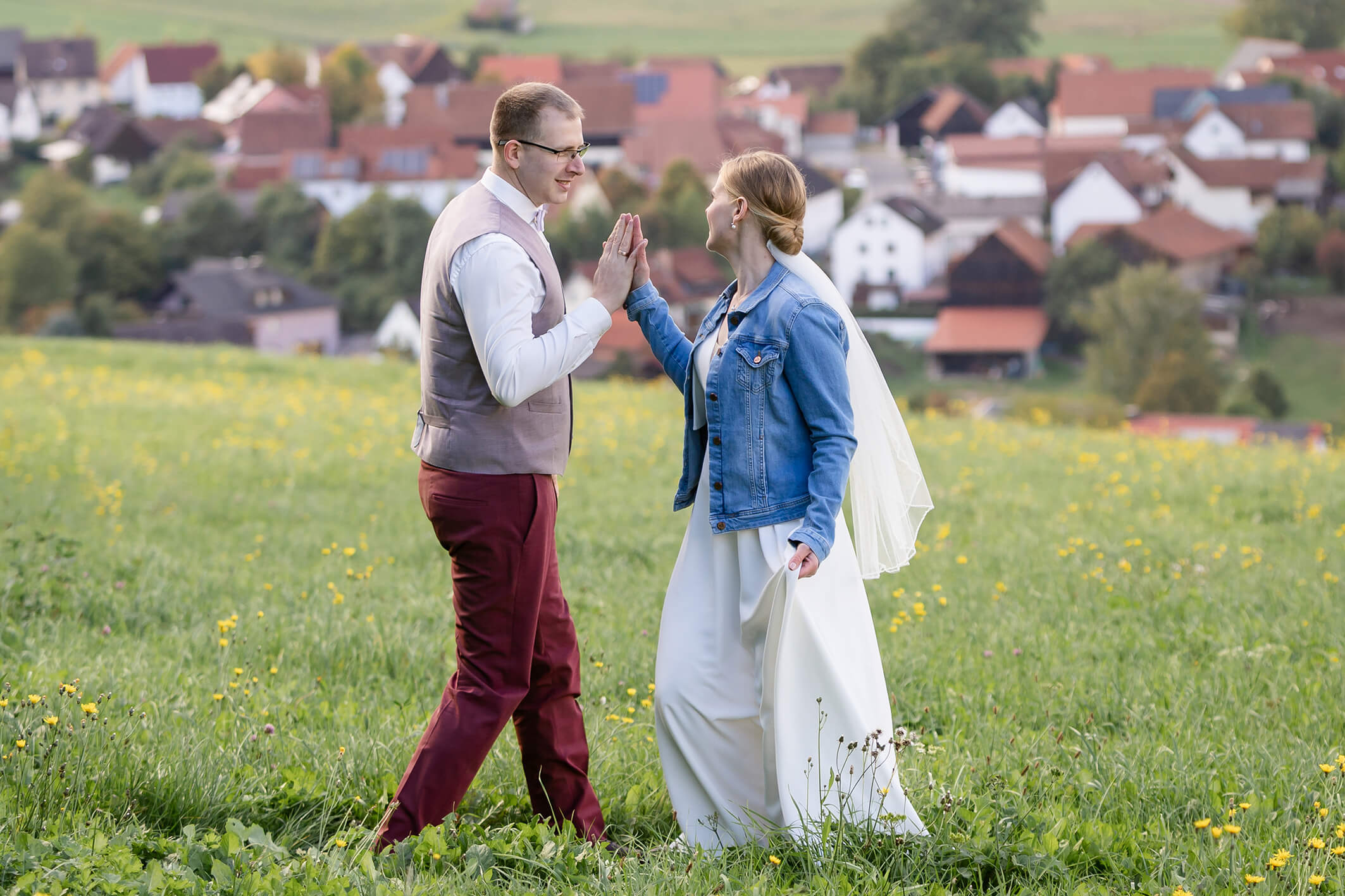 Brautpaar läuft entspannt über eine Wiese, das Kleid der Hochzeitstanz auf der Wiese, Braut schwingt im Wind, lockere natürliche Szene.