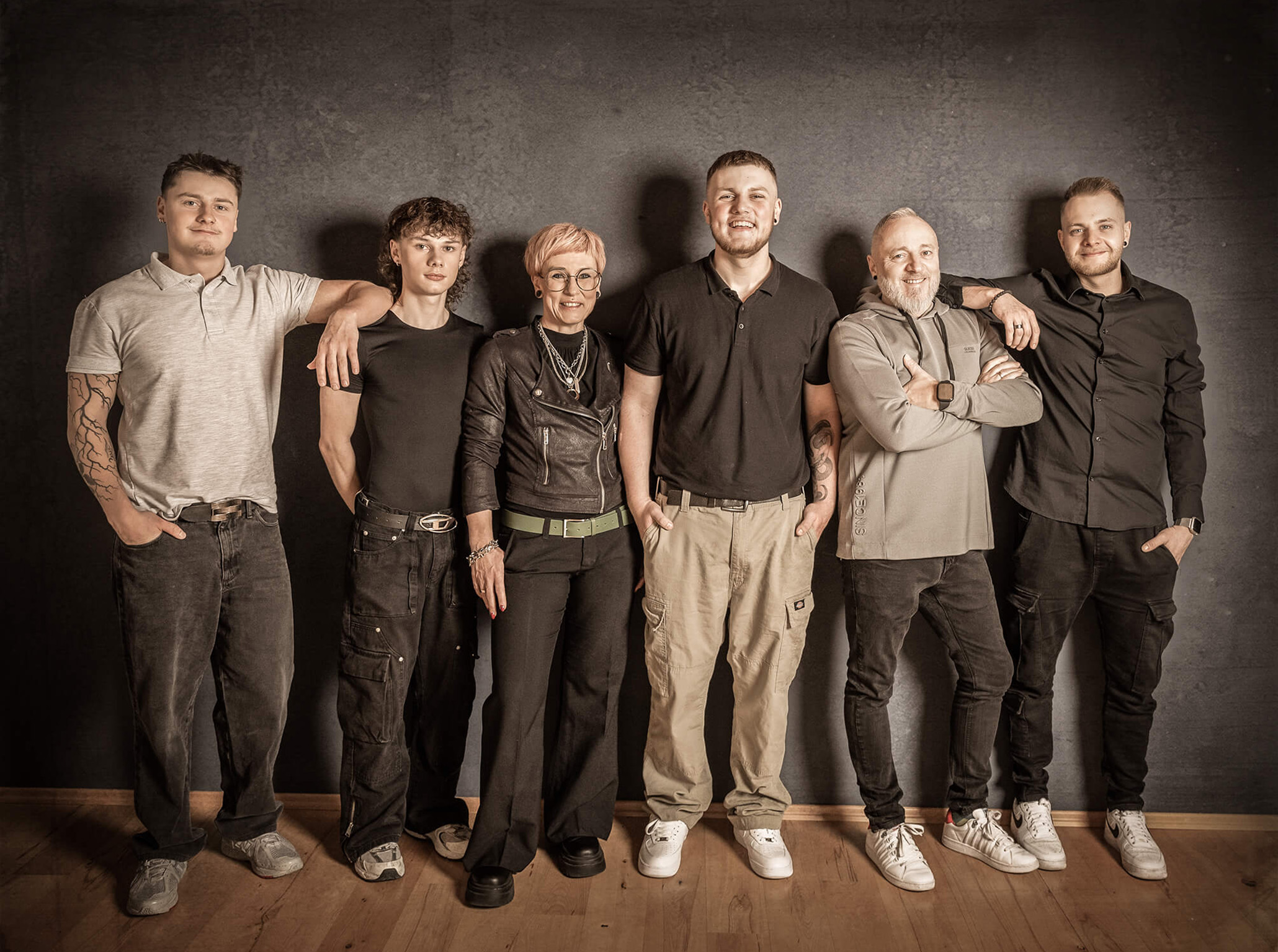 Gemeinsam-familyportrait-doris-dörfler-fotostudio-lichtblick Familie mit vier Söhnen lehnt an einer Wand, ruhiges Portrait in gedeckten Farben.