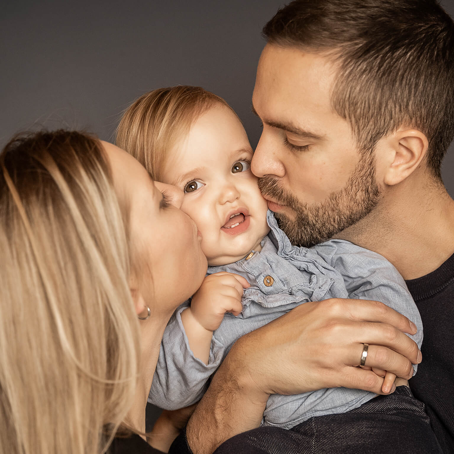Kussfoto-familienliebe-fotostudio-lichtblick-pegnitz-dörfler-quadrat Eltern küssen ihr Baby in der Mitte, liebevolle Familienaufnahme in Farbe.