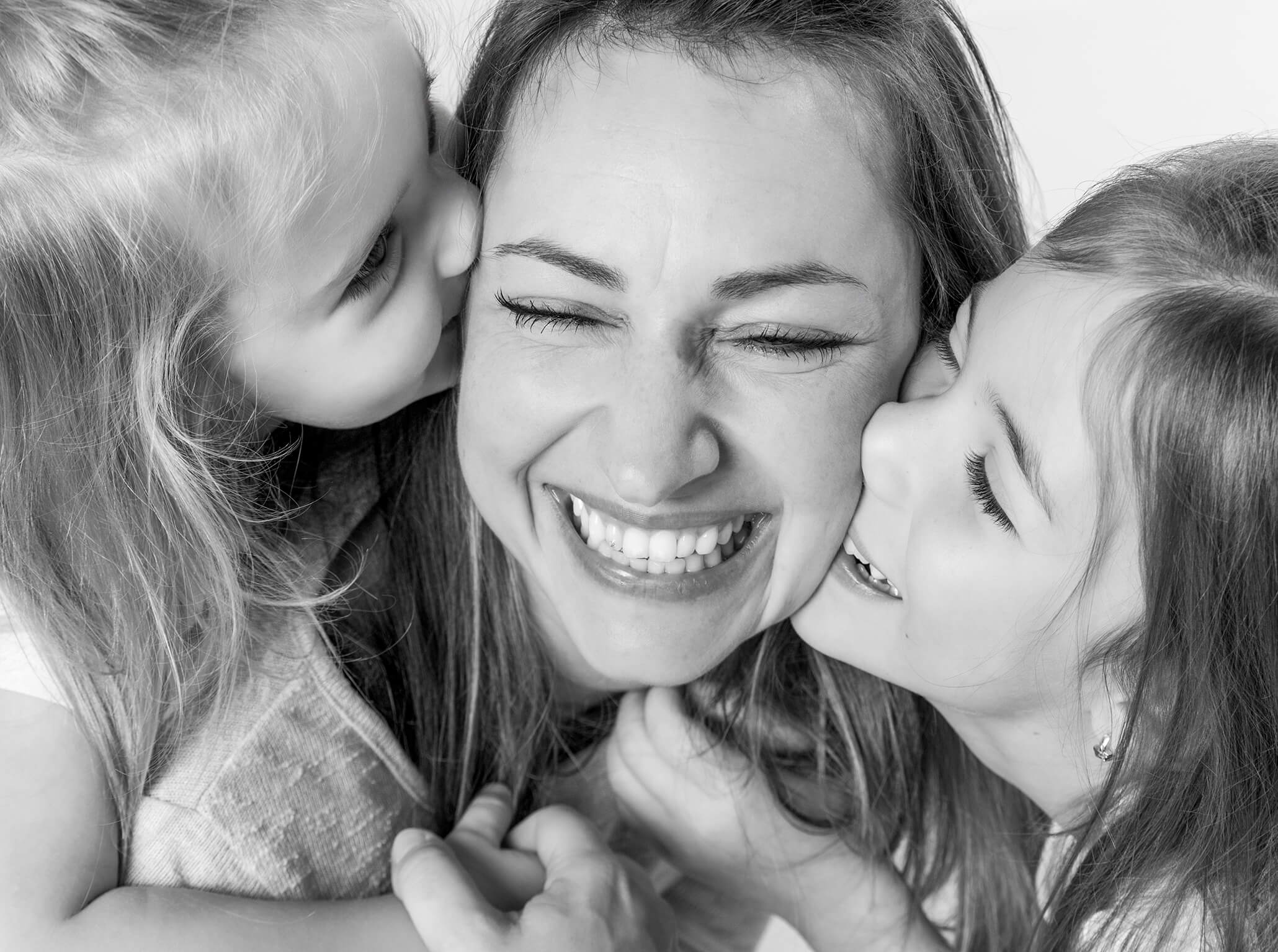Mutter-kind-fotoserie-fotostudio-lichtblick-schwarzweiss Mama liegt im Studio mit ihren Kindern, die sie küssen, schwarz weiß Familienportrait.