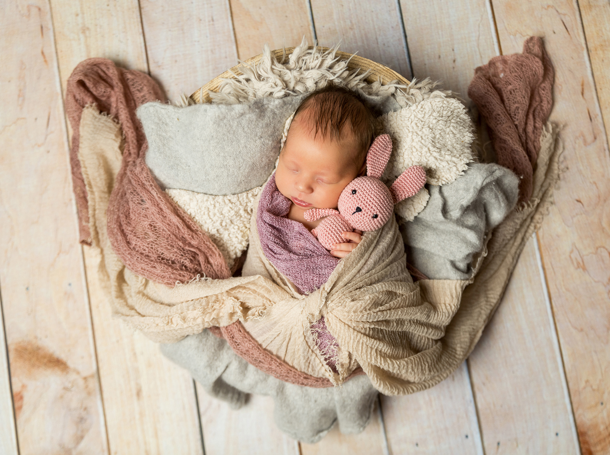 Neugeborenes Baby liegt in einer Holzschale und hält einen kleinen Hasen in den Händen
