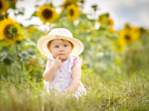Kleines Mädchen sitzt in der Wiese mit Sonnenhut und wirkt schüchtern, Kinderfotografie Outdoor.