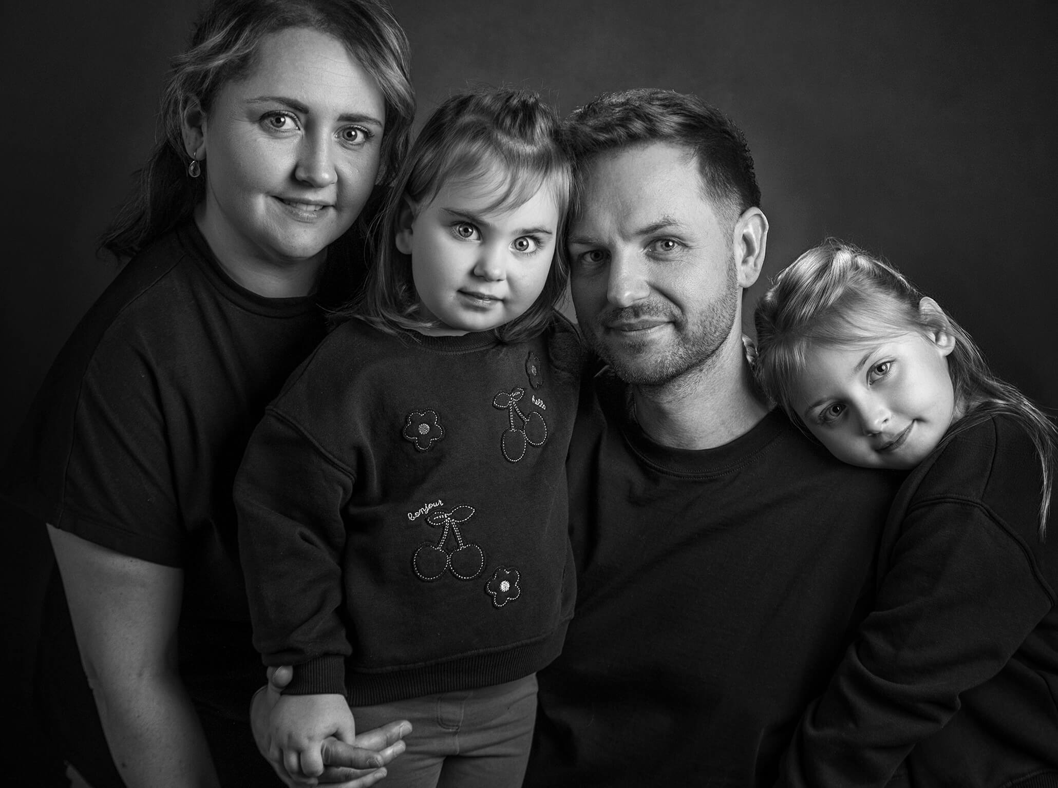familienfoto-monochrome-schwarzweiss-doris-dörfler-fotostudio-lichtblick Schwarz weiß Familienportrait mit vier Personen, dunkler Hintergrund und ruhige Stimmung.