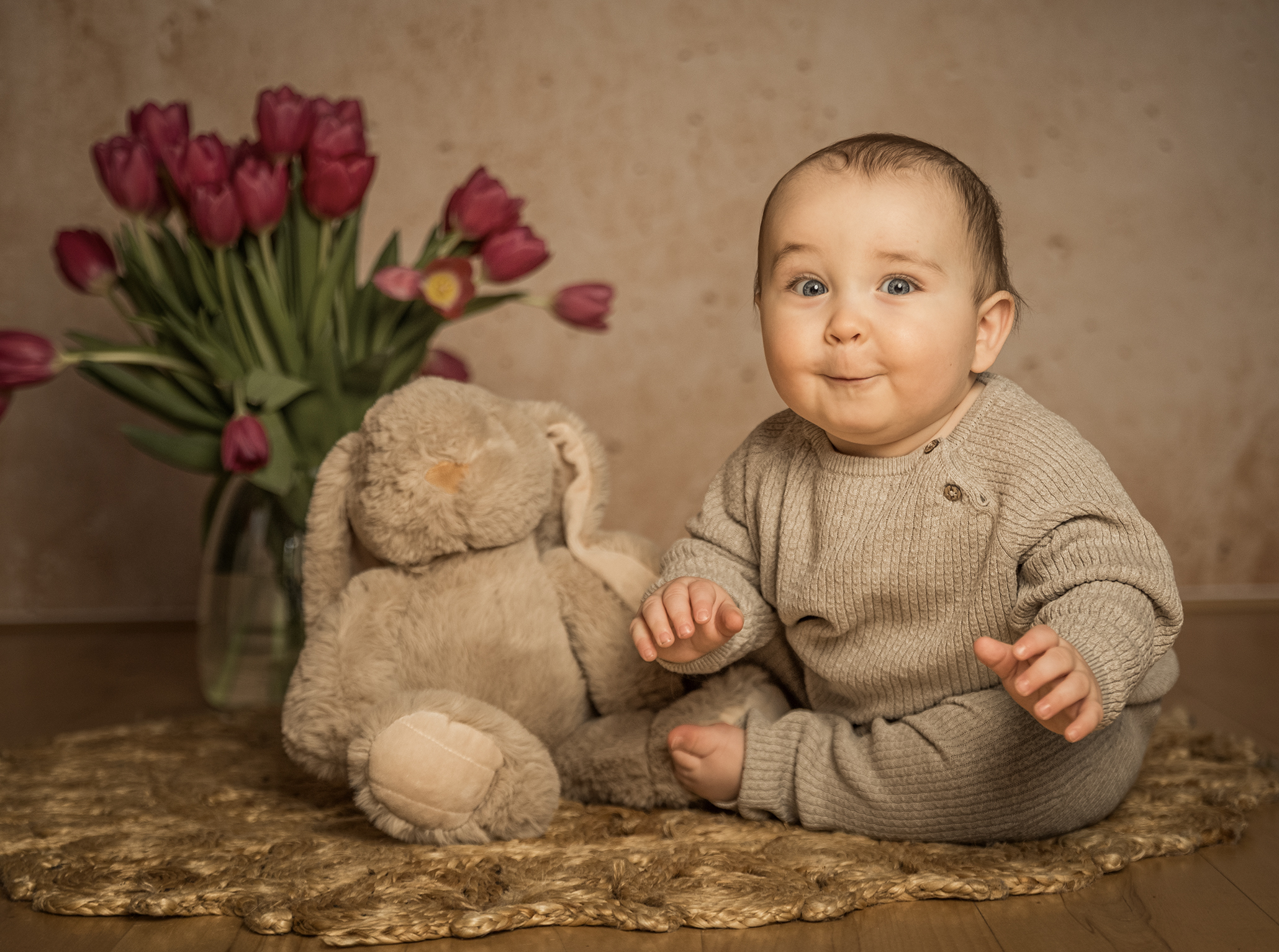 baby sitzt auf em boden und macht ein lustiges Gesicht im Hintergrund sind Tulpen