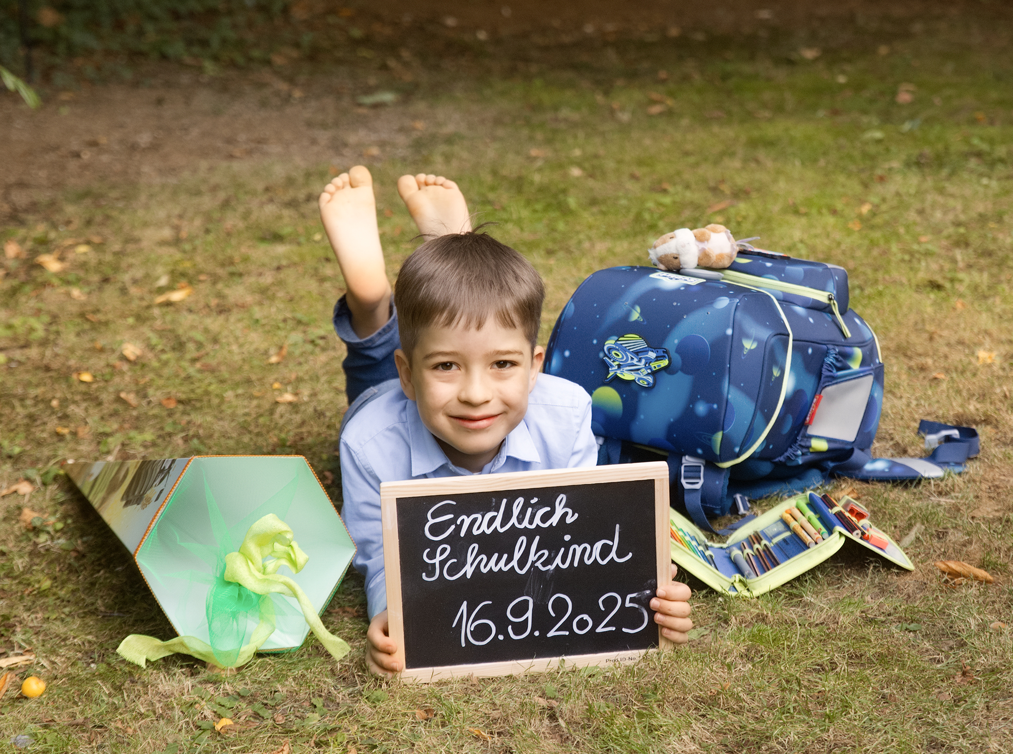 Schulanfangfotos-Doris-Dörfler-mein-erster-Schultag-Fotostudio-Lichtblick-Pegnitz Schulanfangfoto im Garten Junge liegt au dem Boden und hält eine kleine Tafel fet auf der steht Endlich Schulkind